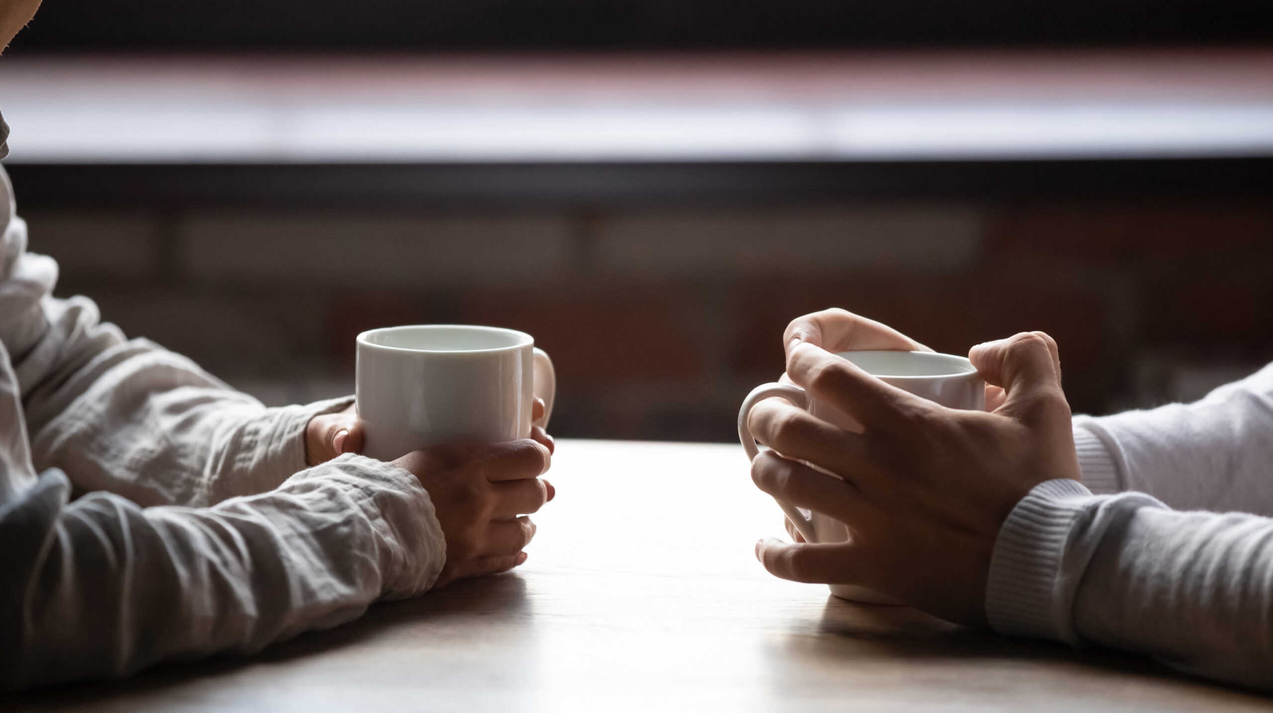 Close up of two people holding coffee cups having a conversation in a cafe about mental health